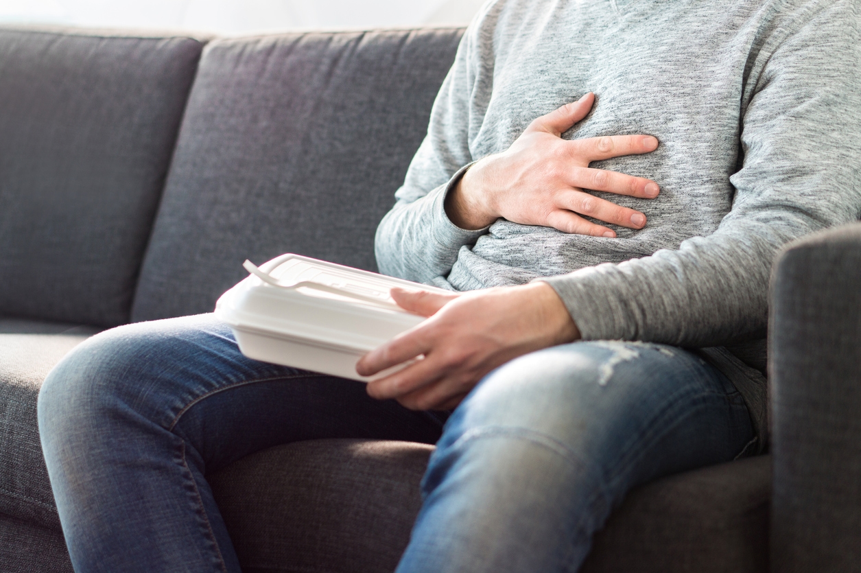 Comment soulager les éructations excessives et les reflux gastriques ? 1 stomach pain, food poisoning or digestion problem after fast junk food. man ate too much and is holding belly with hand.