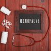 blackboard with text "menopause", stethoscope, pills on blue wooden background