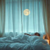 réveils nocturnes : personne éveillée dans son lit au milieu de la nuit, chambre plongée dans une lumière bleutée