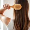 pousse des cheveux : femme brossant doucement ses longs cheveux châtains à la lumière naturelle d'une fenêtre